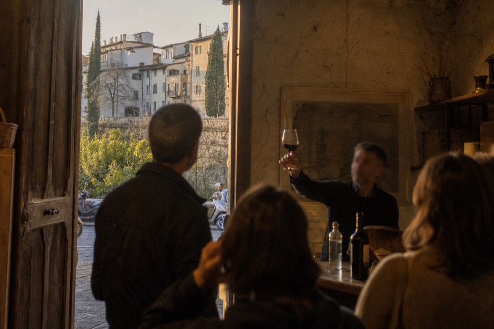 A guide holding up a glass of Tuscan red wine for a small group at a Florence tasting counter