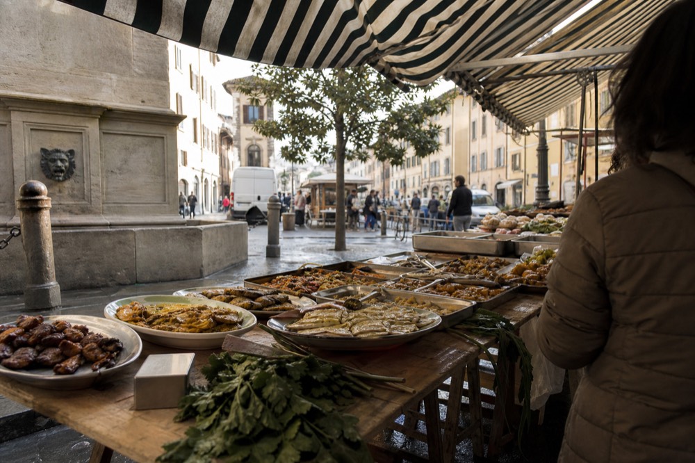 Open-air Florence food stall with trays of prepared dishes under a market awning