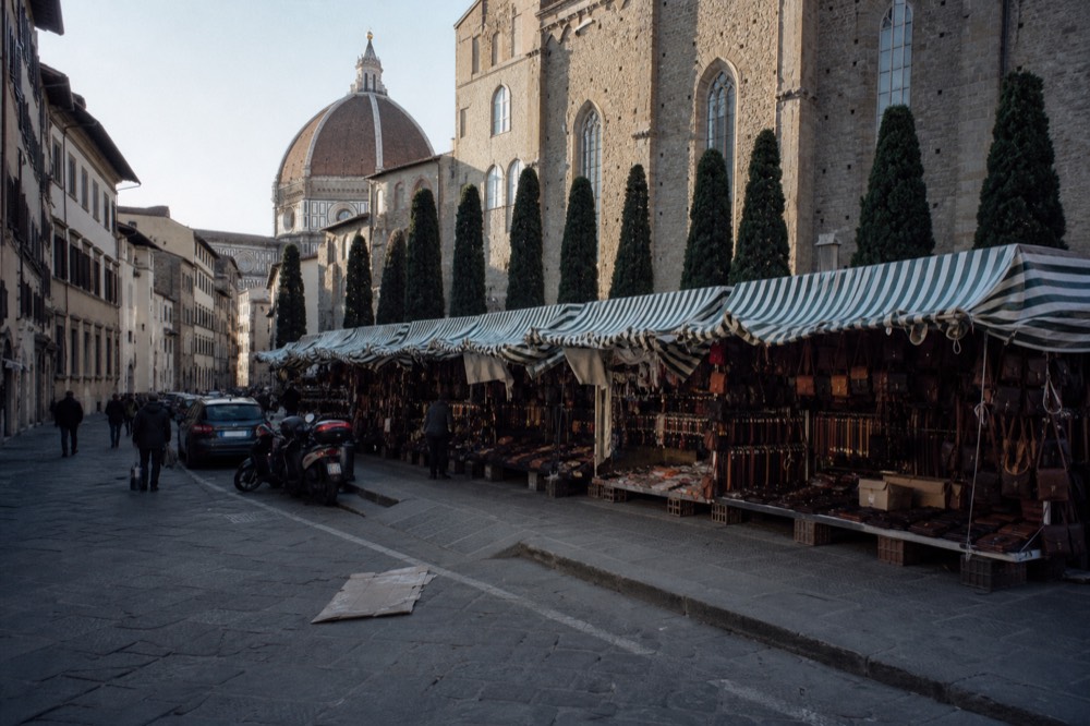 A Florence street with market awnings and a stone tower in spring light
