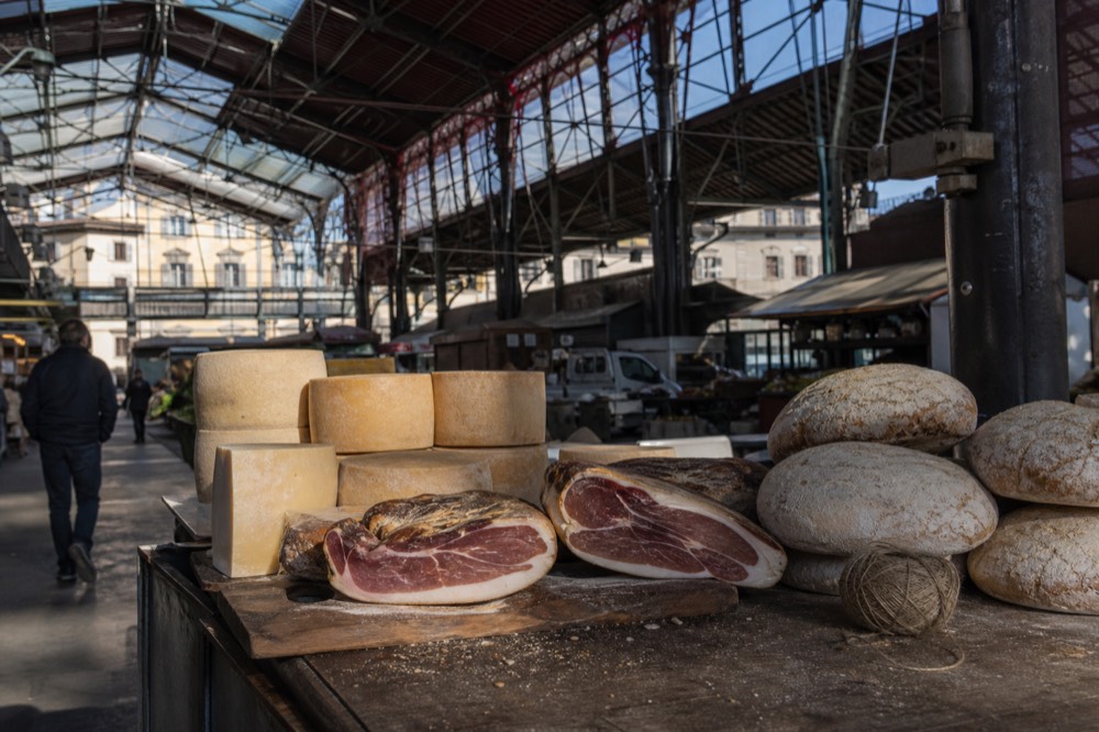 A market stall display of Tuscan cheeses, cured hams and loaves of unsalted bread