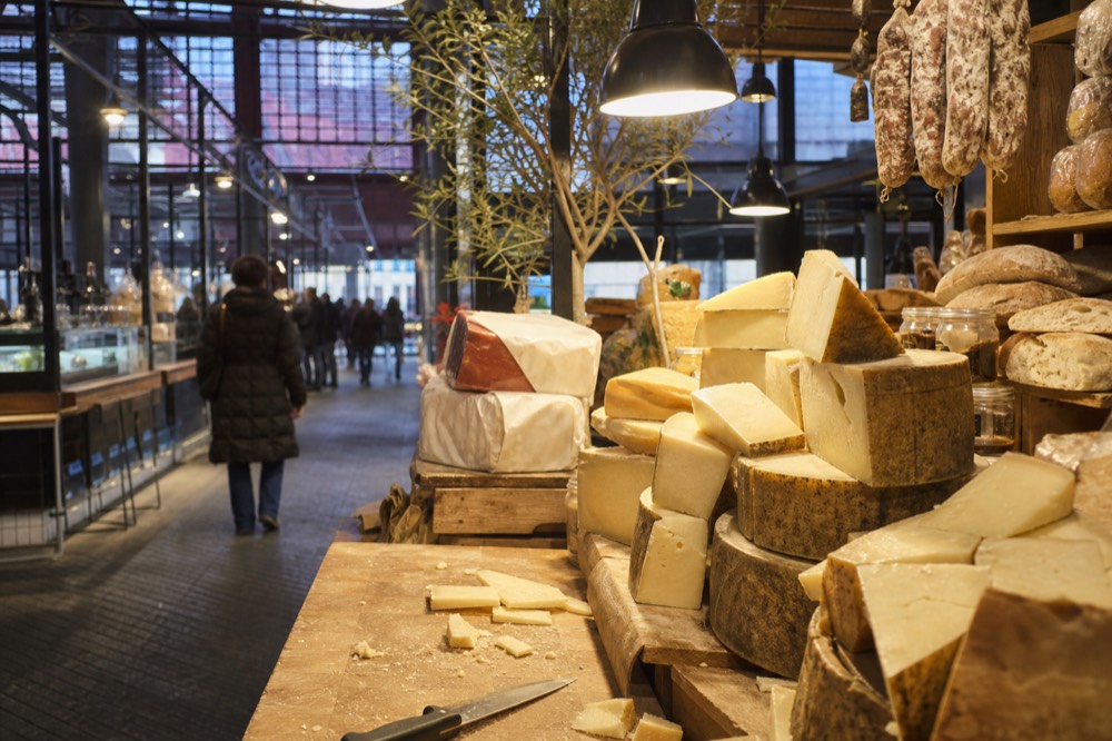 A market food stall with cheeses, cured meats and breads displayed under warm lights