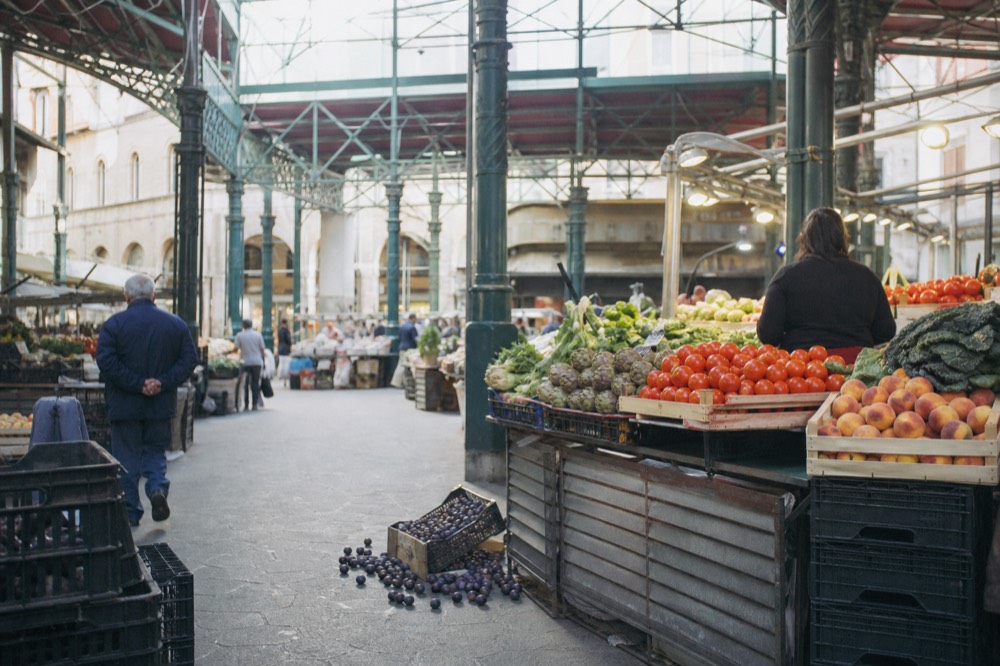 Market stalls piled with fresh produce under the iron and glass roof of a historic market hall