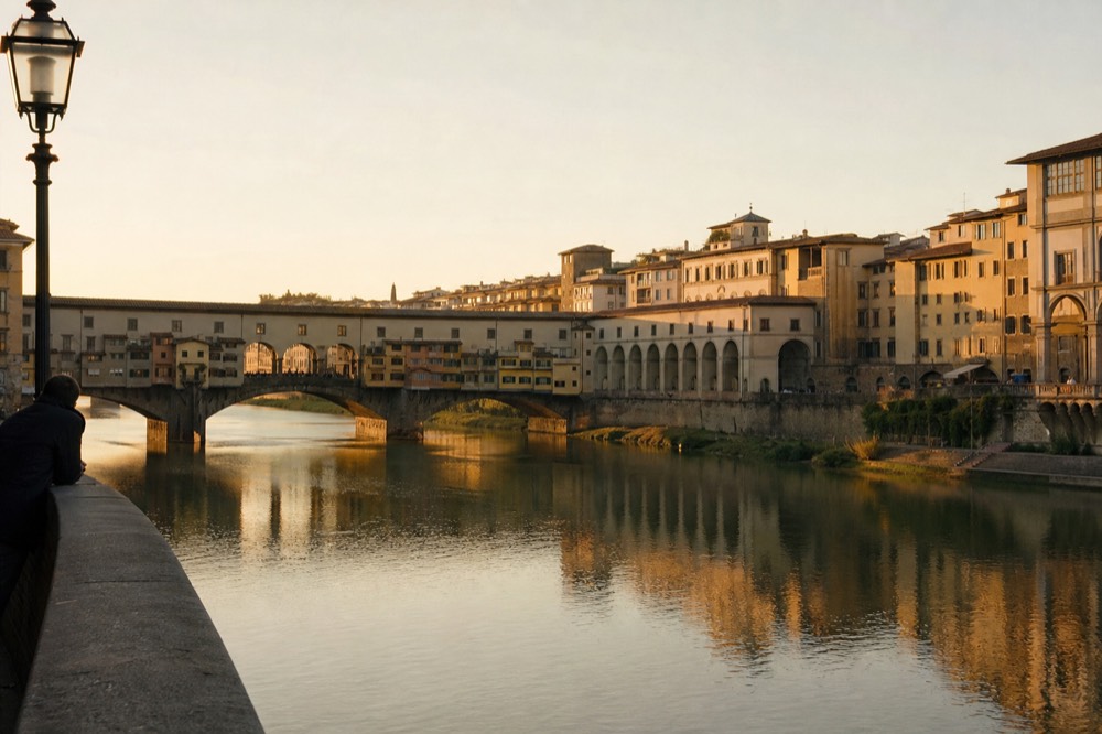 Sunset over the Arno river with bridge arches and riverside buildings reflected in the water
