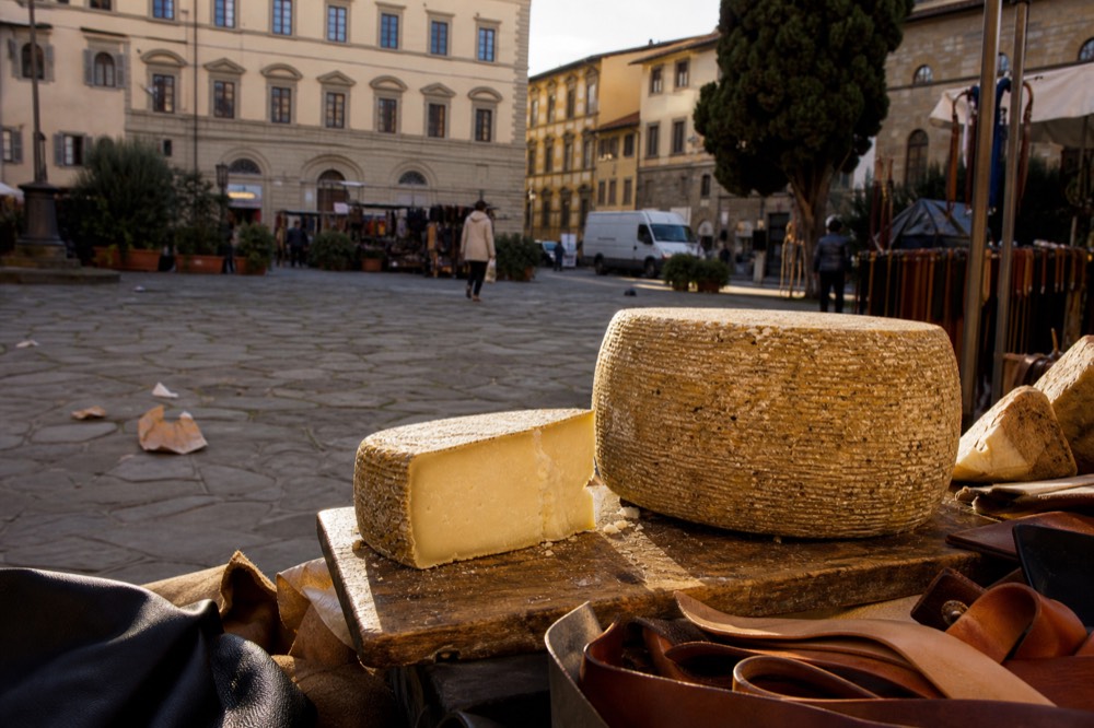 Wheel of aged pecorino cheese and a wedge cut on a wooden board at a market stall