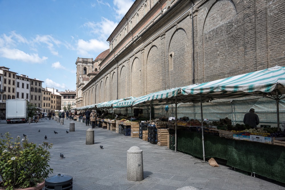 Outdoor market stalls with striped canopies along a Florence street