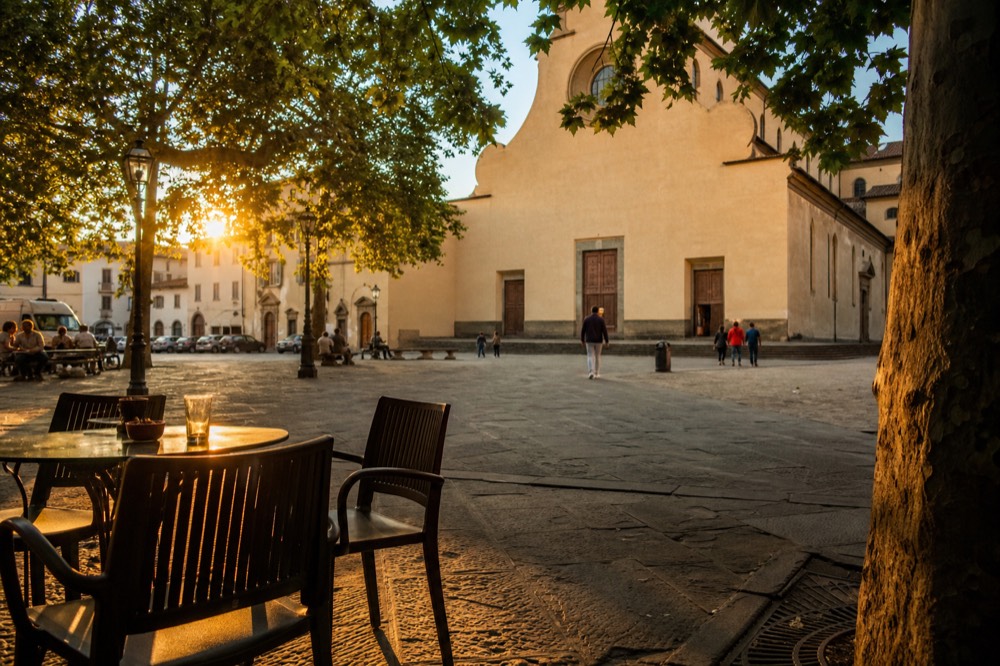 A historic Florentine piazza at golden hour with a church facade and outdoor cafe tables