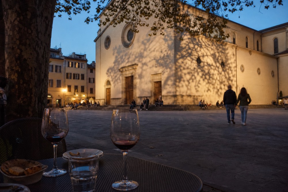 Wine glasses and small plates on a table at dusk beside a Florence square