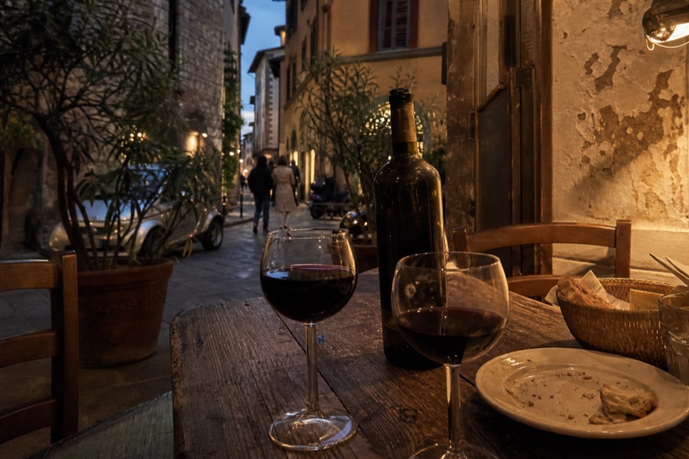 A Tuscan wine bottle and filled glasses on a rustic restaurant table