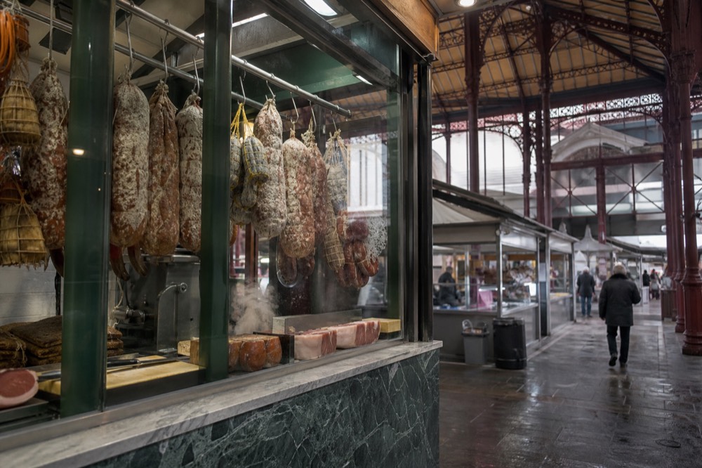 A food stall counter in a Florence market hall with hanging cured meats