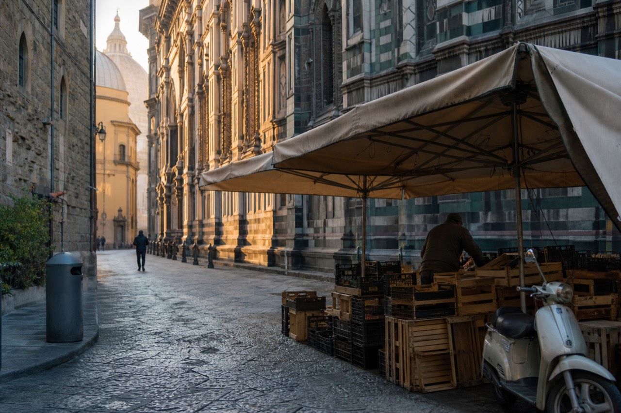 A quiet Florentine street with stone buildings and a market stall in the foreground