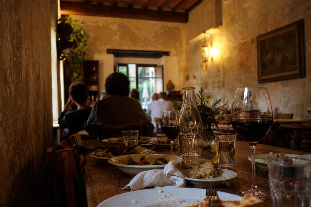 Long table set for dinner inside a warmly lit Florentine trattoria with wine glasses