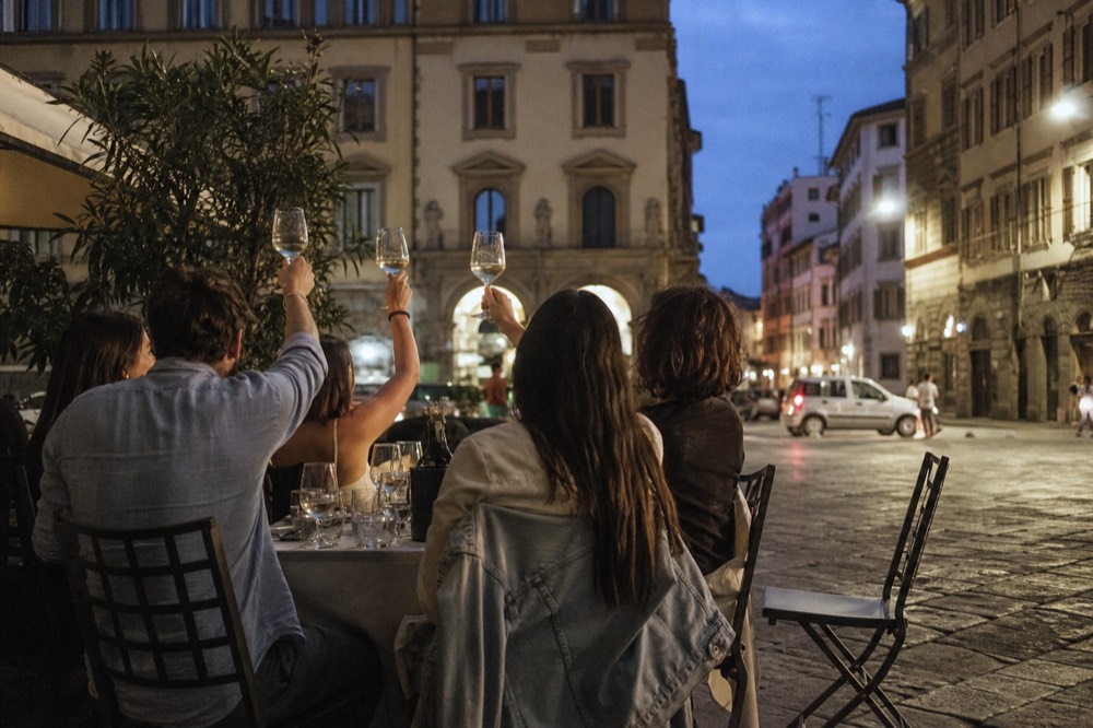 Small group of diners with wine glasses raised in a toast at an outdoor evening table