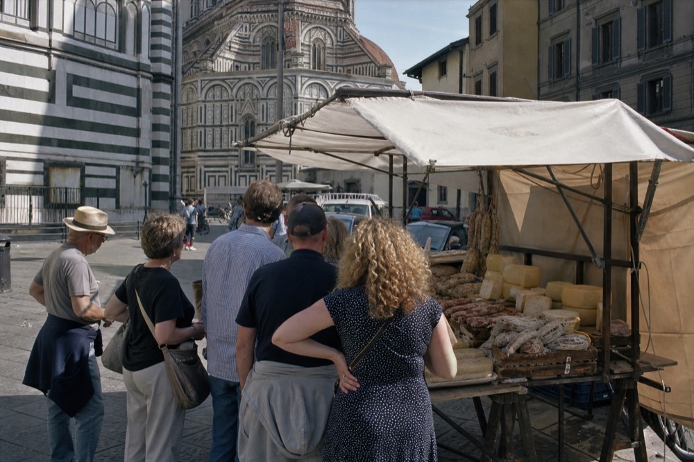 A guided food tour group standing at a market stall with cured meats and cheese on display