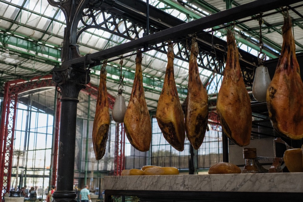 A Florence market counter with whole legs of cured ham hanging from a rack