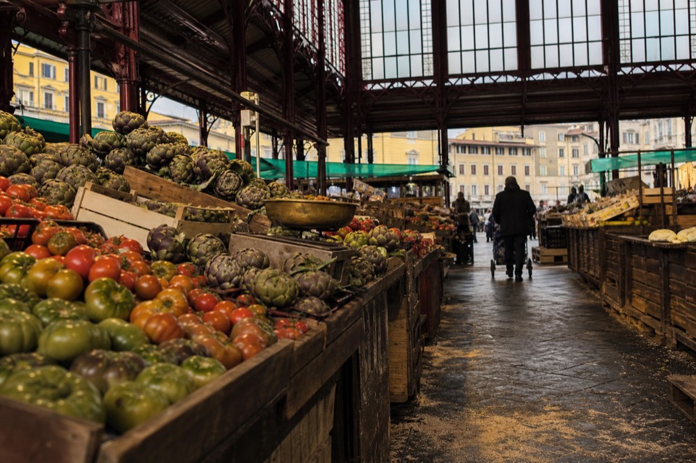 Interior of a historic covered market with produce stalls under a glass and iron roof
