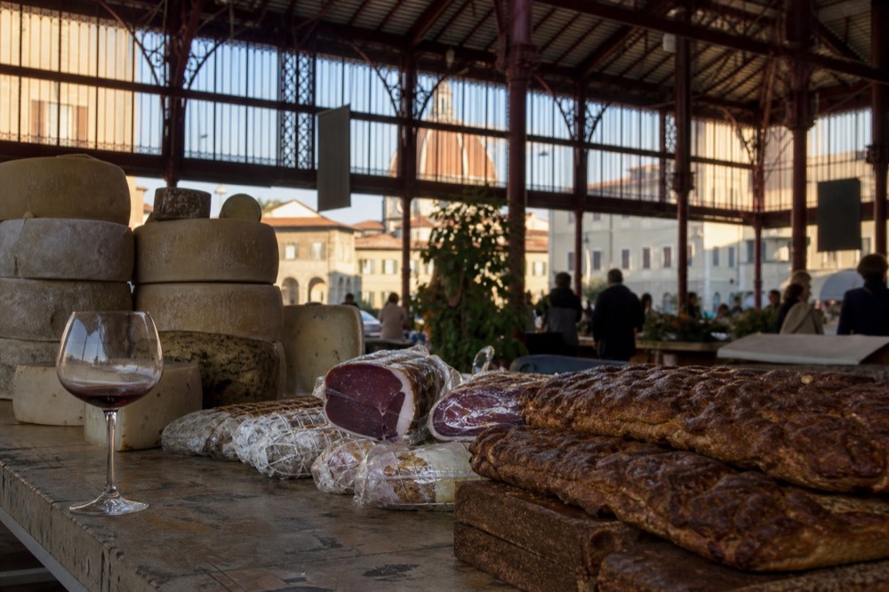 A wooden market counter with cheeses, bread and cured meats