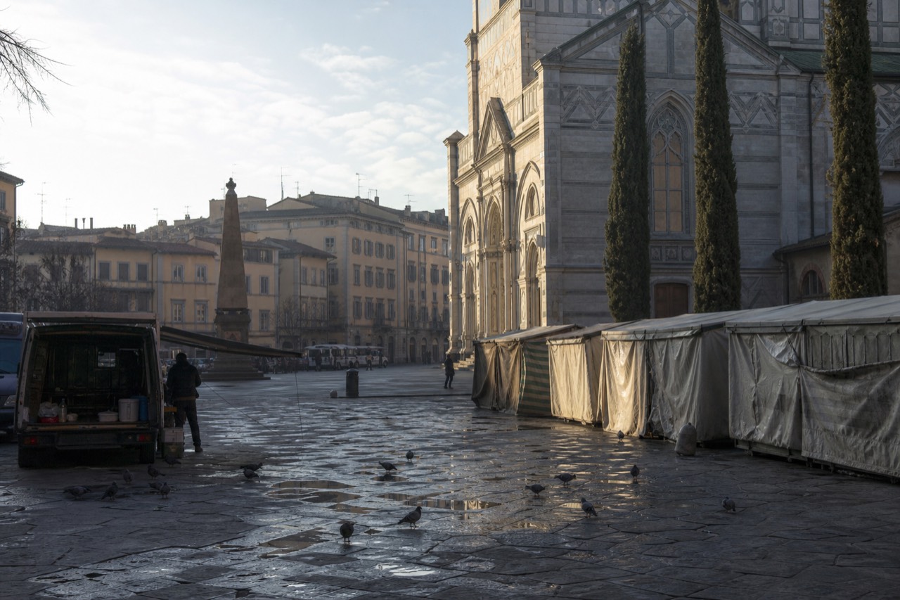 A quiet Florentine piazza at morning with market stalls and old stone buildings