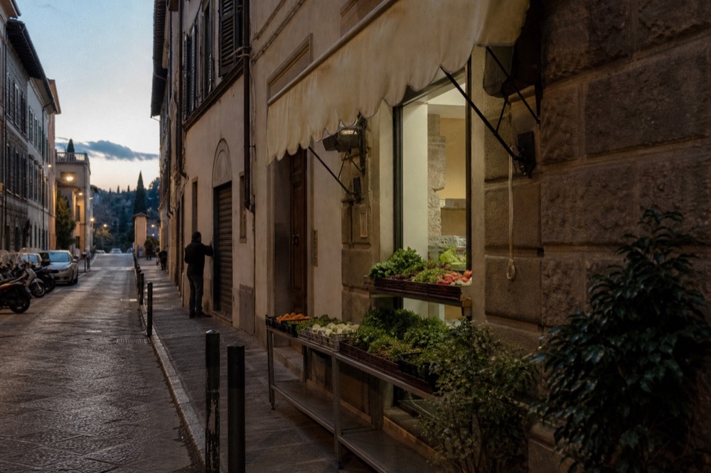 A narrow Florence street with a food shop counter and awning in the historic centre