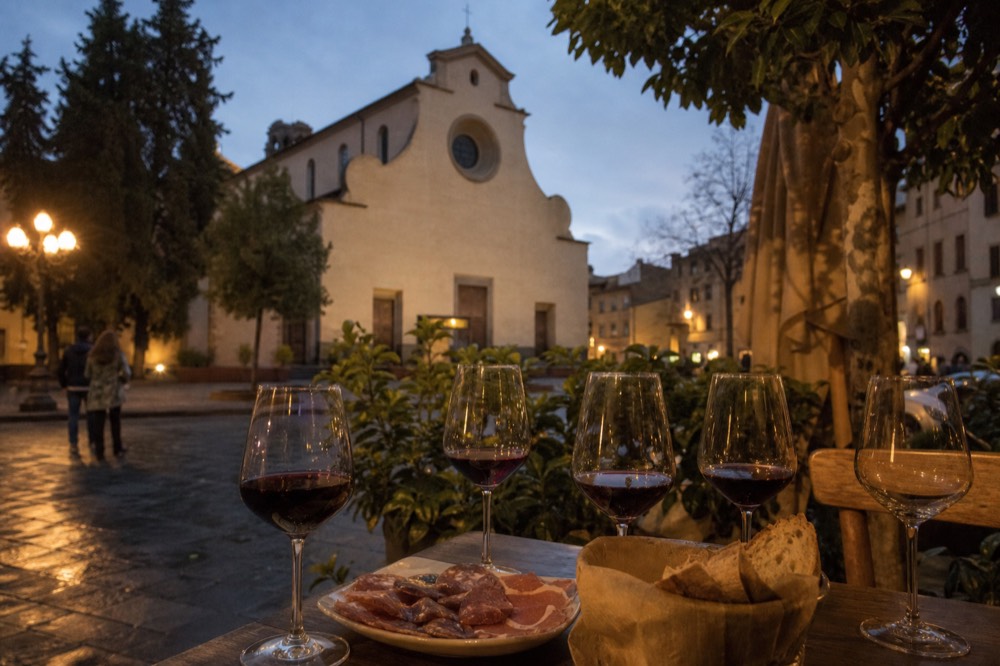 An evening table with glasses of red wine, bread and a plate of Tuscan cured meats