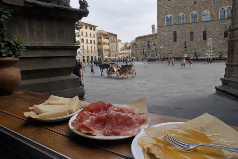Small plates of cheese, salami and honey arranged along a wooden counter