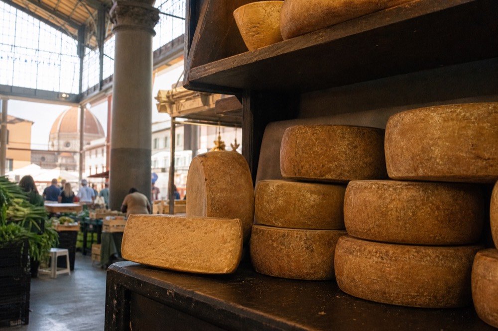 Cheese counter with whole aged pecorino wheels stacked in a market stall