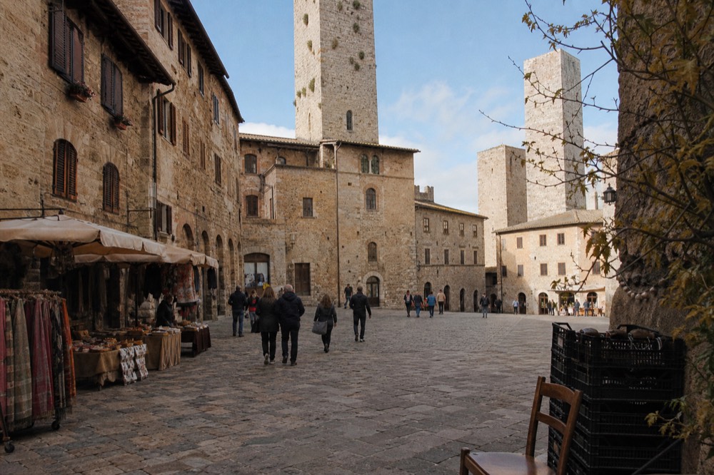 A historic Tuscan hill town square with market stalls and stone buildings