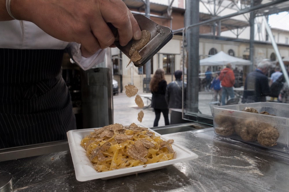 A hand shaving thin slices of white truffle over a bowl of pasta