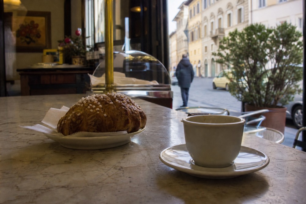 A marble bar counter in a Florence cafe with an espresso cup and a cornetto on a saucer
